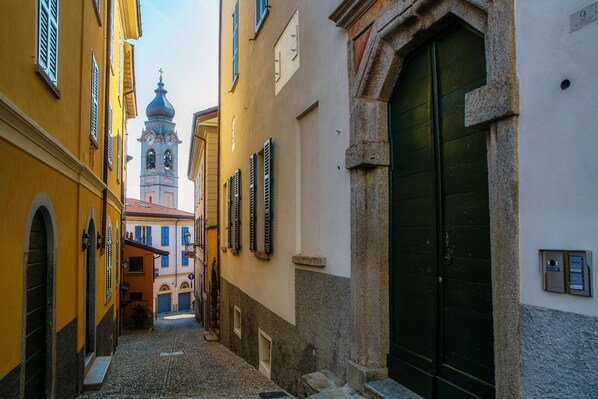 Una estrecha calle adoquinada flanqueada por edificios, una puerta verde y una torre del reloj a lo lejos.