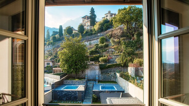 Une vue depuis un balcon donnant sur un espace piscine, avec un mur en pierre et une colline parsemée de bâtiments.