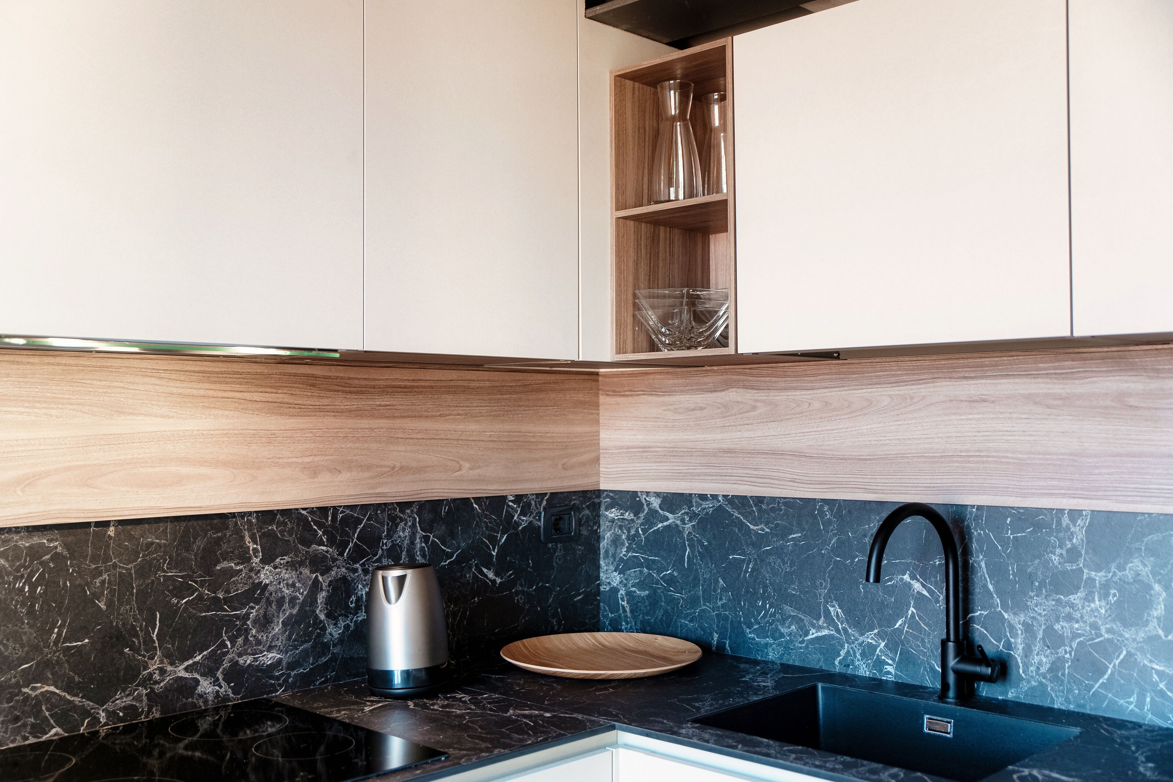 Cocina moderna con salpicadero de mármol negro, lavamanos negro y estante de madera sobre la encimera.