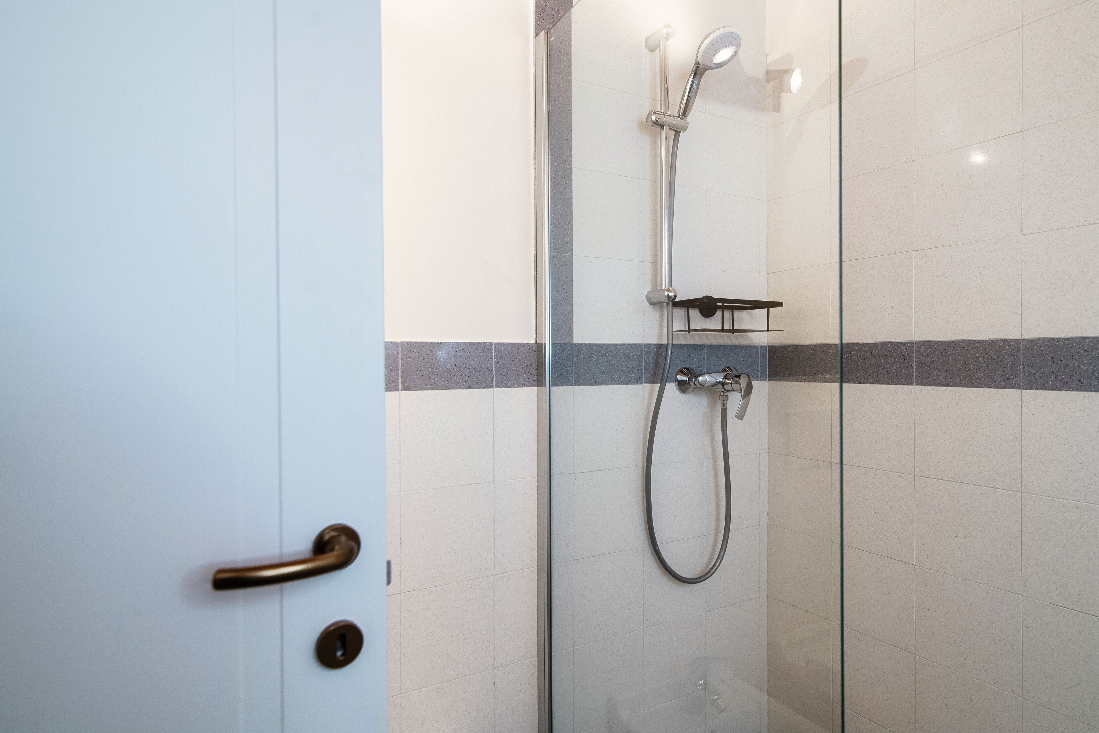 A glass-enclosed shower area with a handheld showerhead and a wall-mounted faucet.