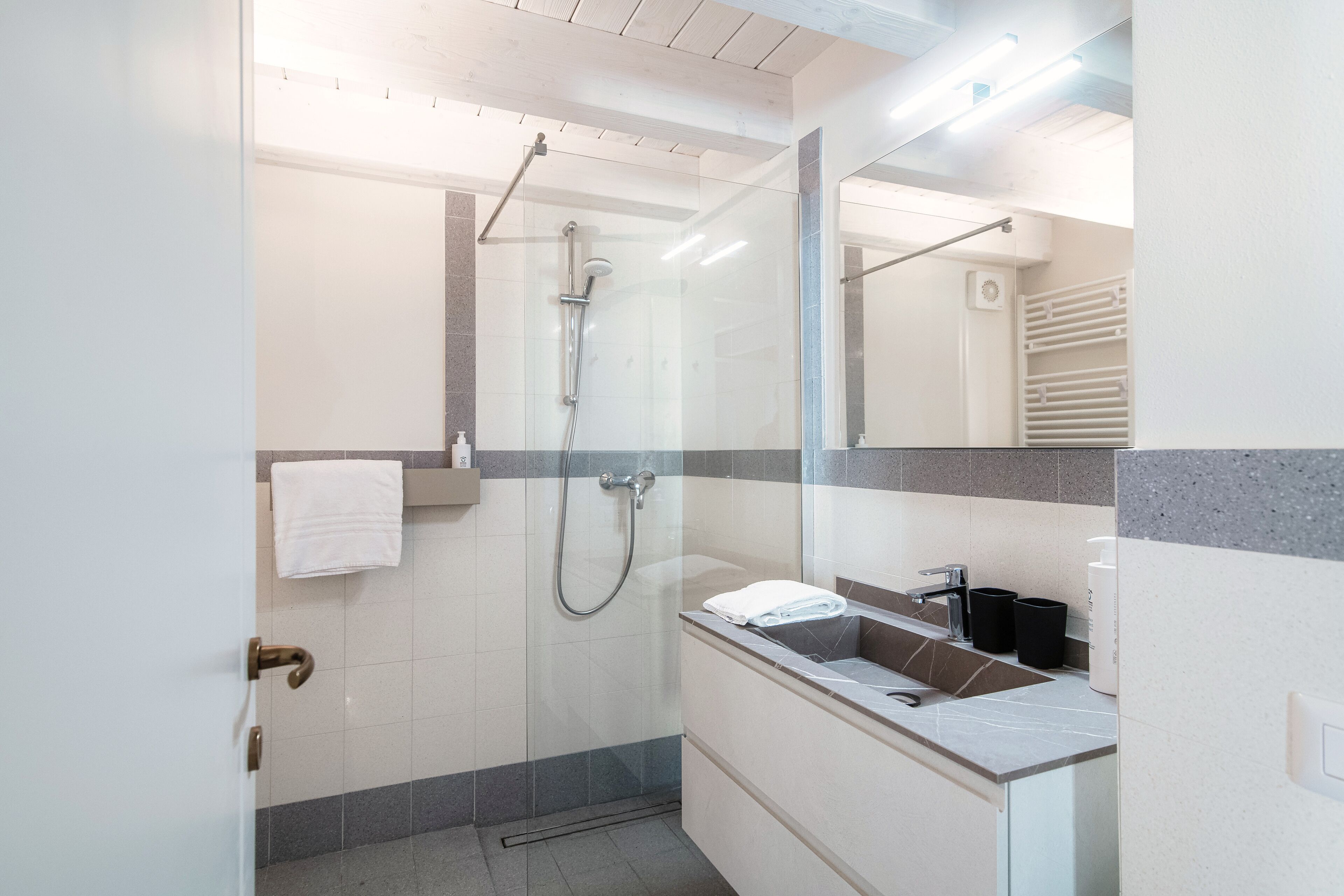 A modern bathroom with a glass-enclosed shower, a white sink with a mirror, and a towel rack.