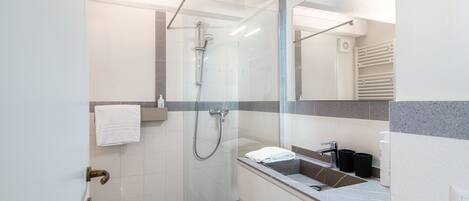 A modern bathroom with a glass-enclosed shower, a white sink with a mirror, and a towel rack.