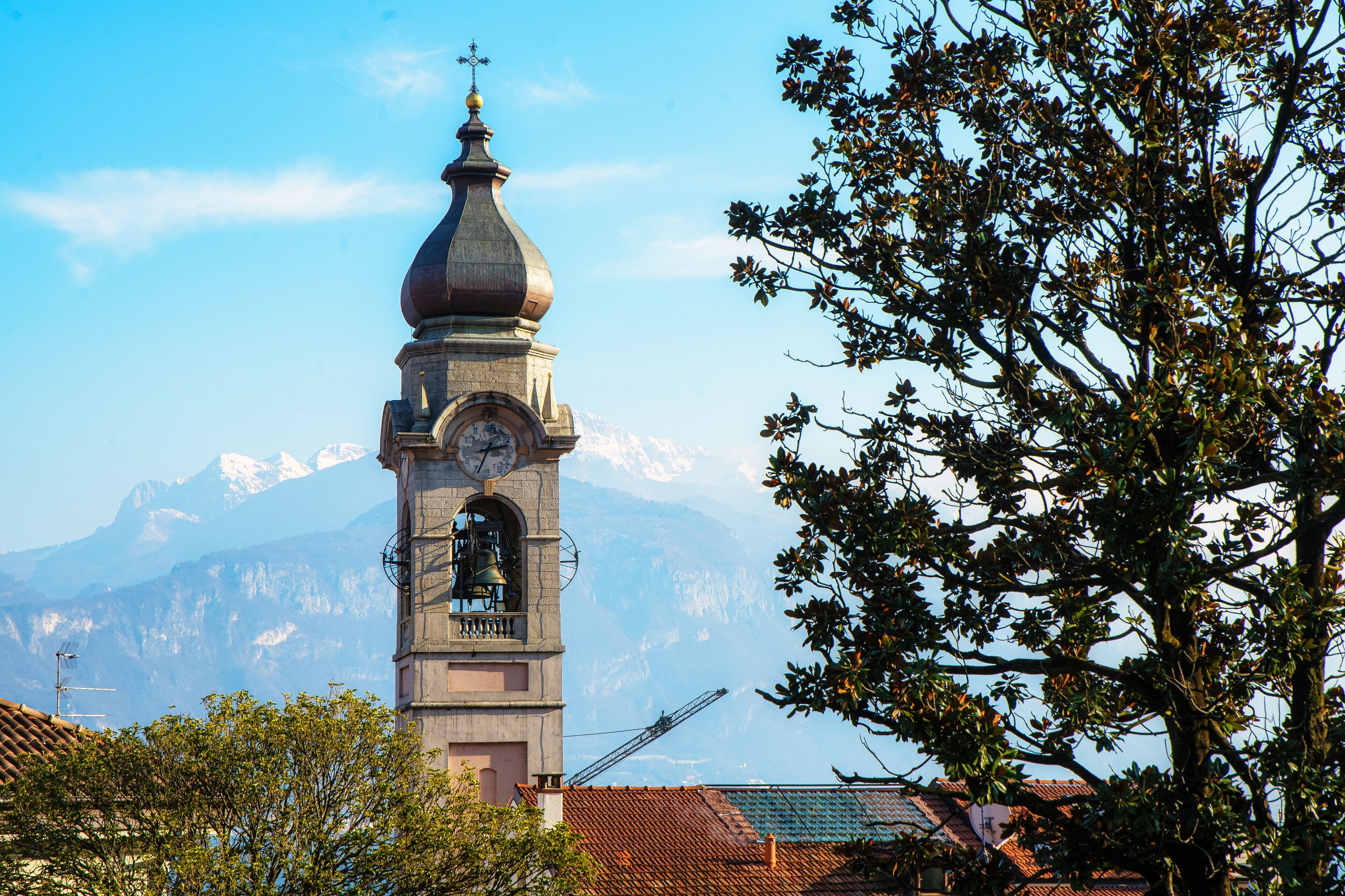 Ein Glockenturm, umgeben von Bäumen und Gebäuden, mit Bergen im Hintergrund.
