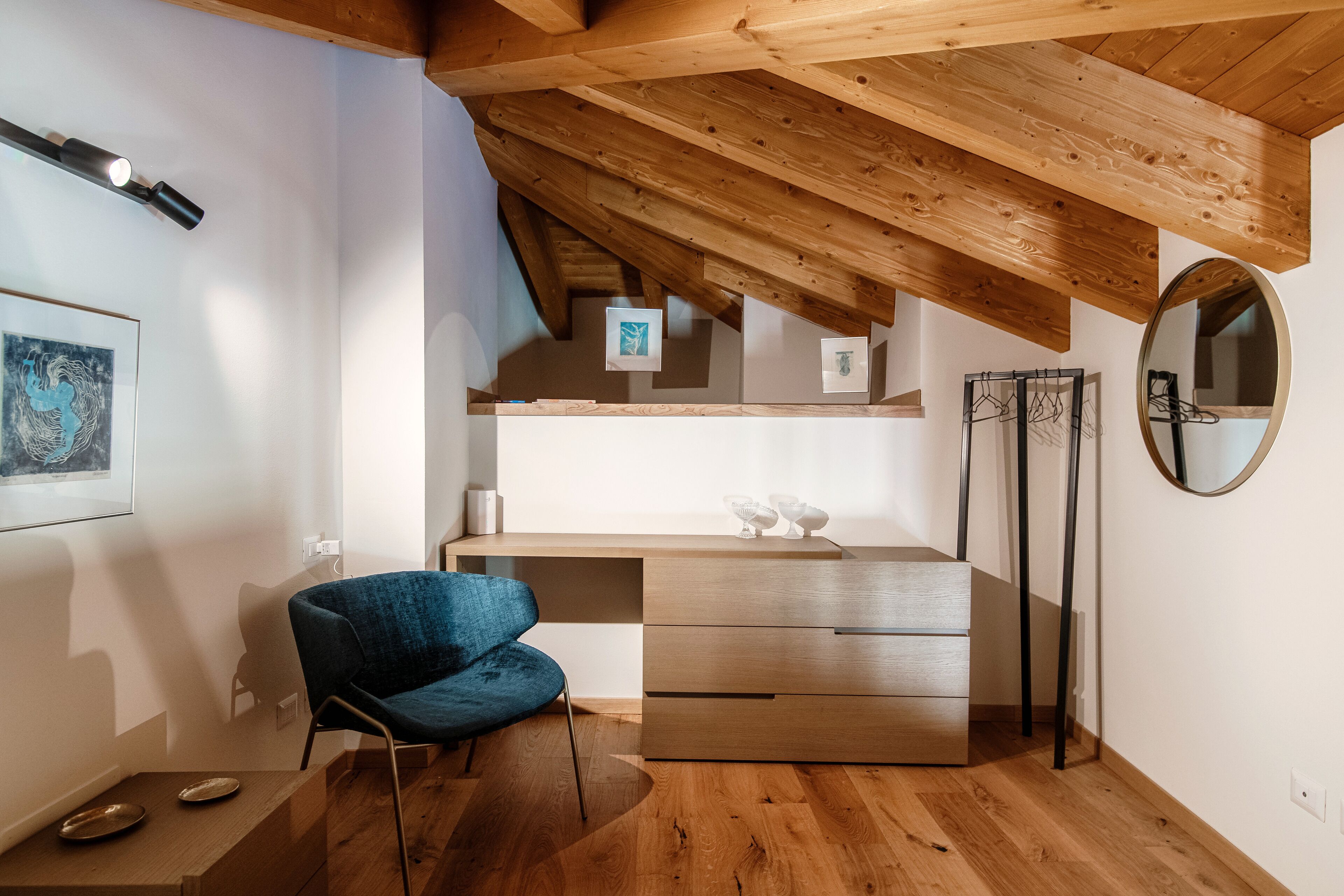 Ein stilvolles, kleines Zimmer mit Holzboden, einem blauen Stuhl, einem Holztisch und einem Spiegel.
