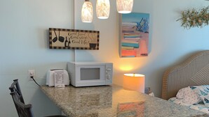 A kitchen with a granite countertop, a microwave, a toaster, and a hanging light fixture. - Ocean Front Studio Condo on Treasure Island (Treasure Island)