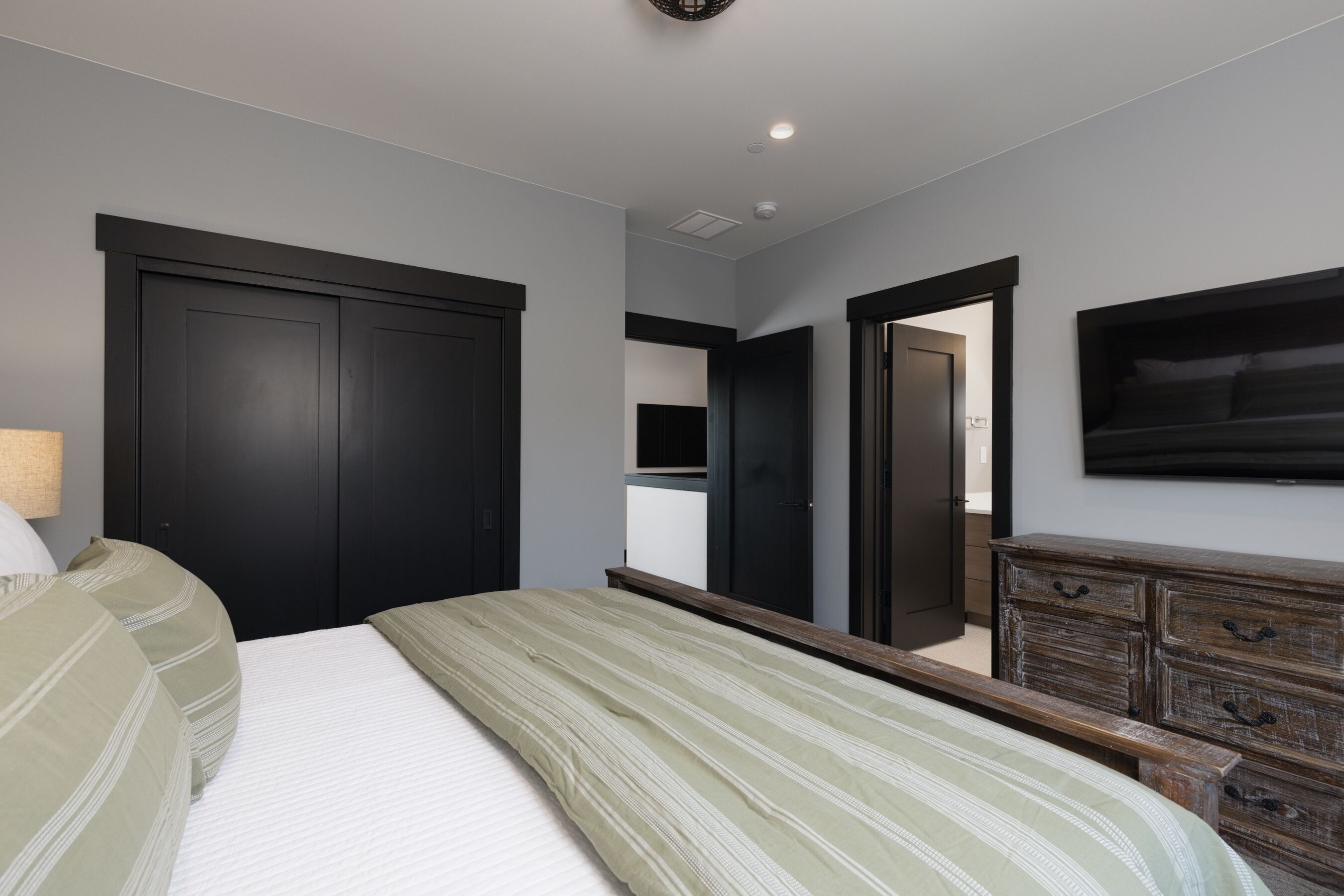 Un dormitorio con cama, cómoda, espejo y televisor montado en la pared.