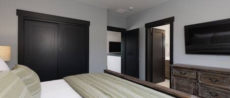 Un dormitorio con cama, cómoda, espejo y televisor montado en la pared.