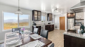 A modern kitchen with dark wood cabinets, a stainless steel refrigerator, and a dining area with a view of the outdoors. - Point Arena Lighthouse - Assistant Keeper's House 4 (Point Arena)