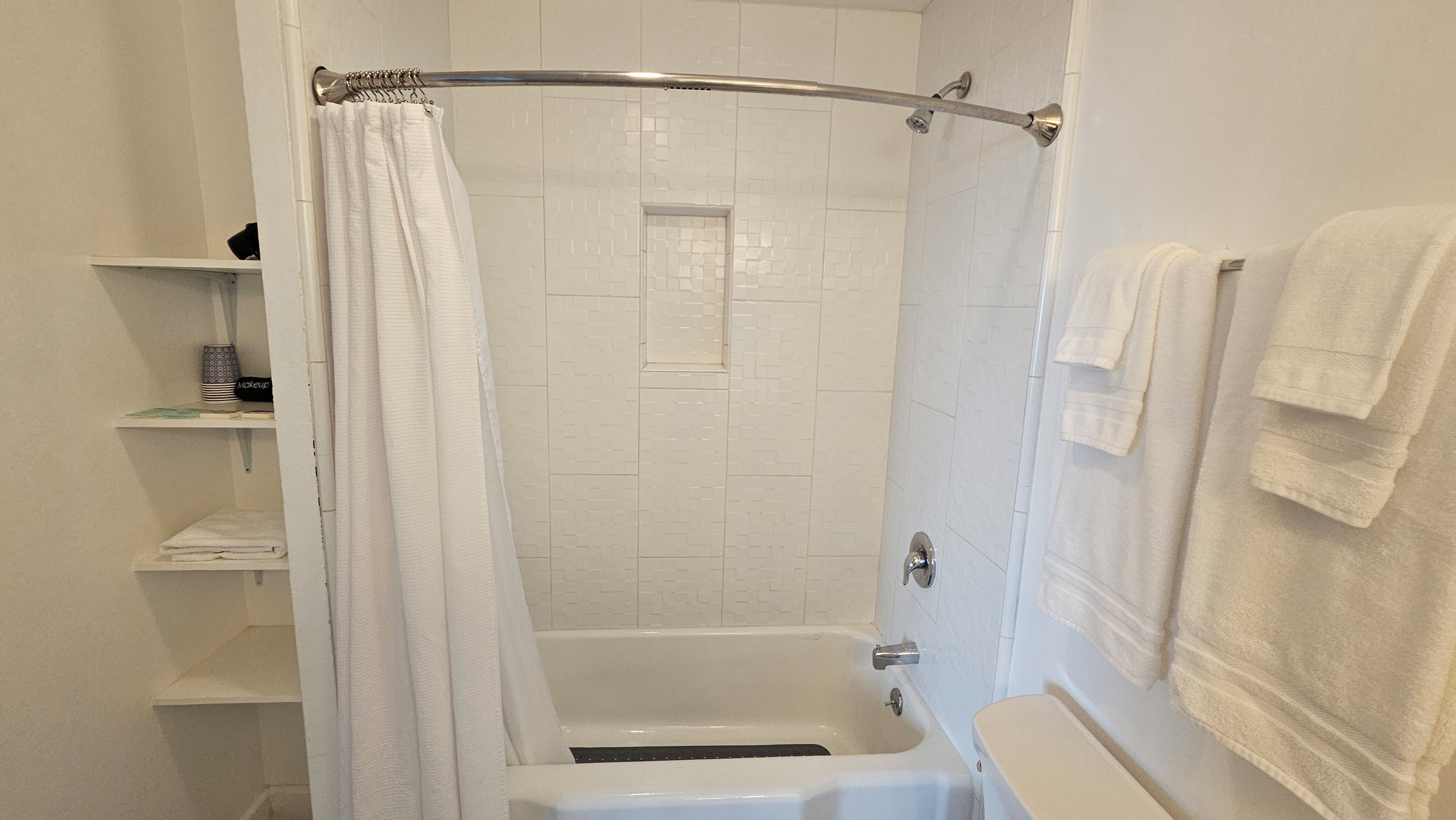 A bathroom with a shower, a bathtub, and a toilet. There are white towels hanging on the wall and a shower curtain.