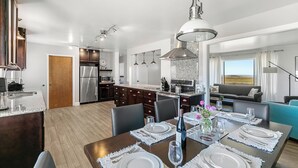 A modern kitchen with dark cabinets, stainless steel appliances, and a dining area set for six with white tableware and a wine bottle. - Point Arena Lighthouse - Assistant Keeper's House 4 (Point Arena)