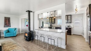 A modern kitchen with a central island, bar stools, and a wood-burning stove. - Point Arena Lighthouse - Assistant Keeper's House 4 (Point Arena)