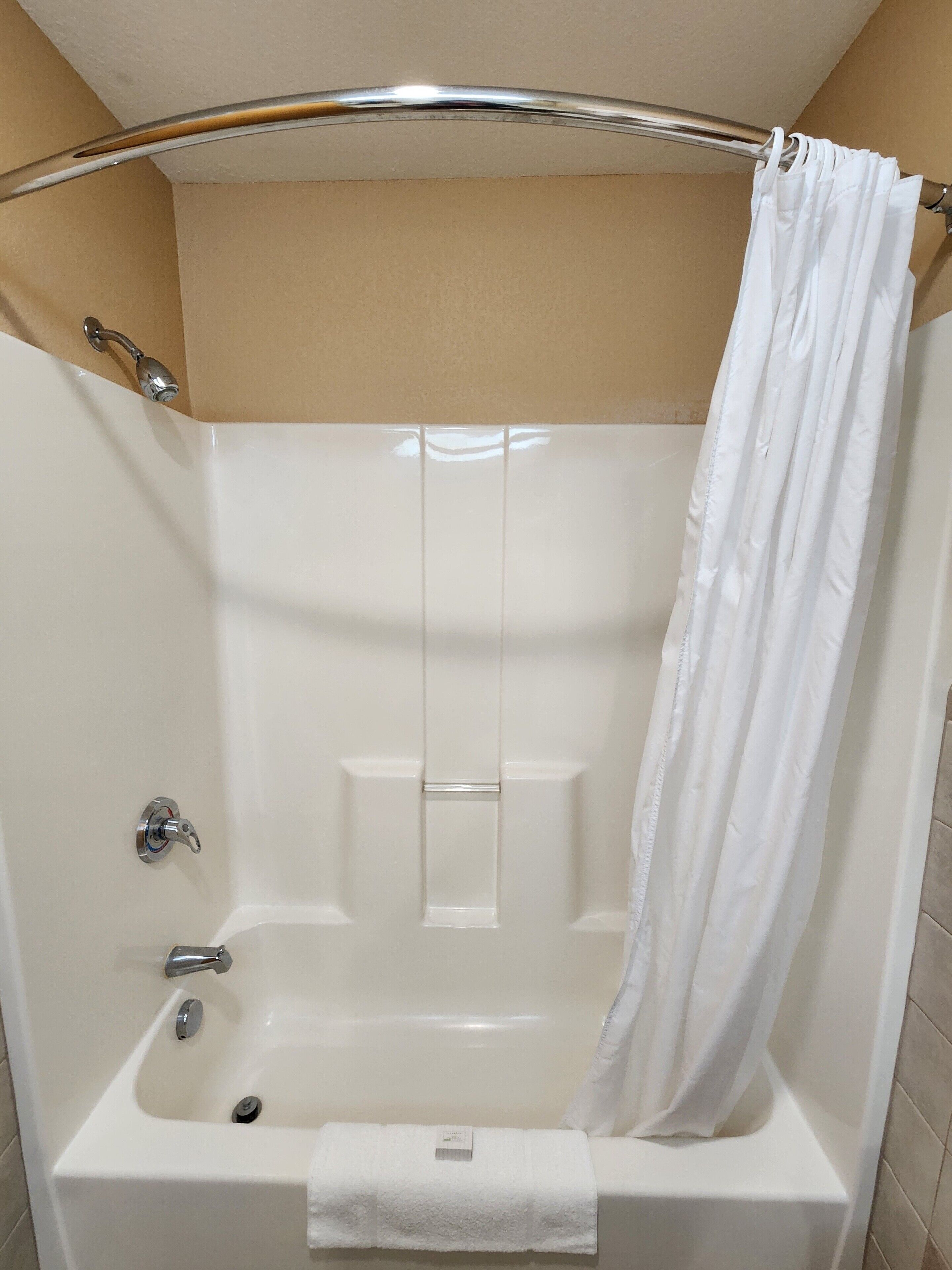 A white bathtub with a shower curtain, a towel, and a chrome faucet.