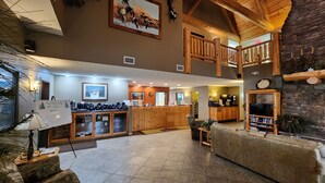 A spacious lobby with a high ceiling, wooden beams, a reception desk, a kitchen area, and a seating area with a television. - Pine Peaks Lodge & Suites (Crosslake)