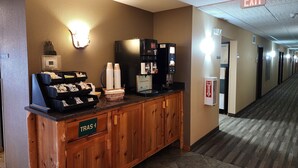 A hotel reception area with a coffee machine, a trash bin, and a sign indicating the direction to the restrooms. - Pine Peaks Lodge & Suites (Crosslake)
