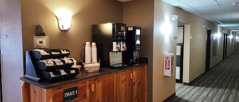 A hotel reception area with a coffee machine, a trash bin, and a sign indicating the direction to the restrooms.