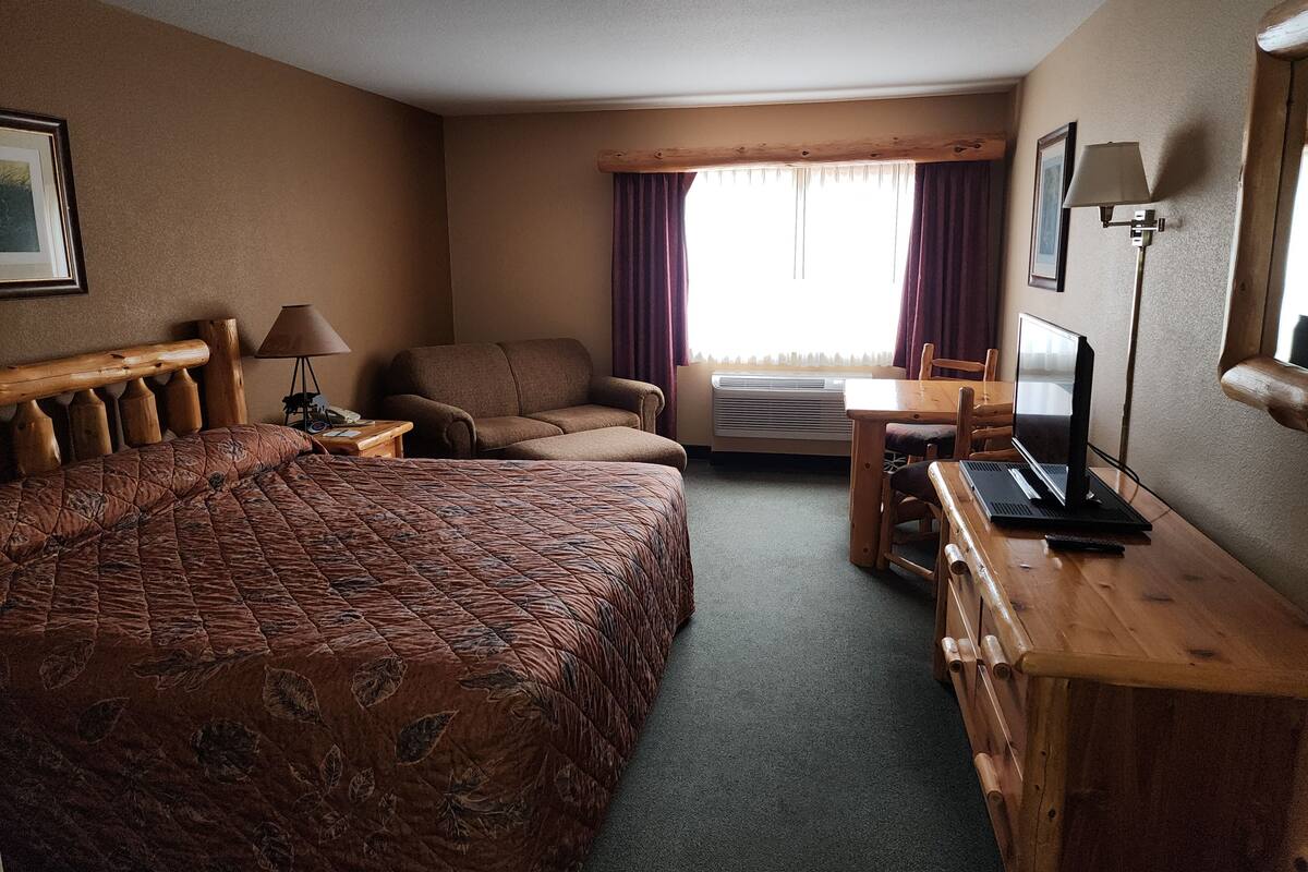 A hotel room with a large bed, a desk with a laptop, a chair, and an air conditioning unit.