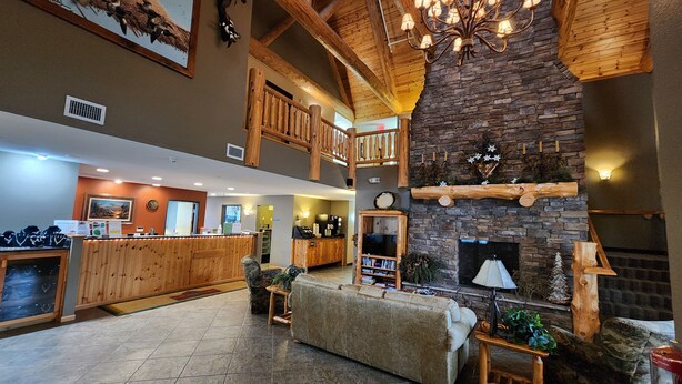 A spacious lobby with a high ceiling, wooden beams, a stone fireplace, a reception desk, and a cozy seating area. - Pine Peaks Lodge & Suites (Crosslake)