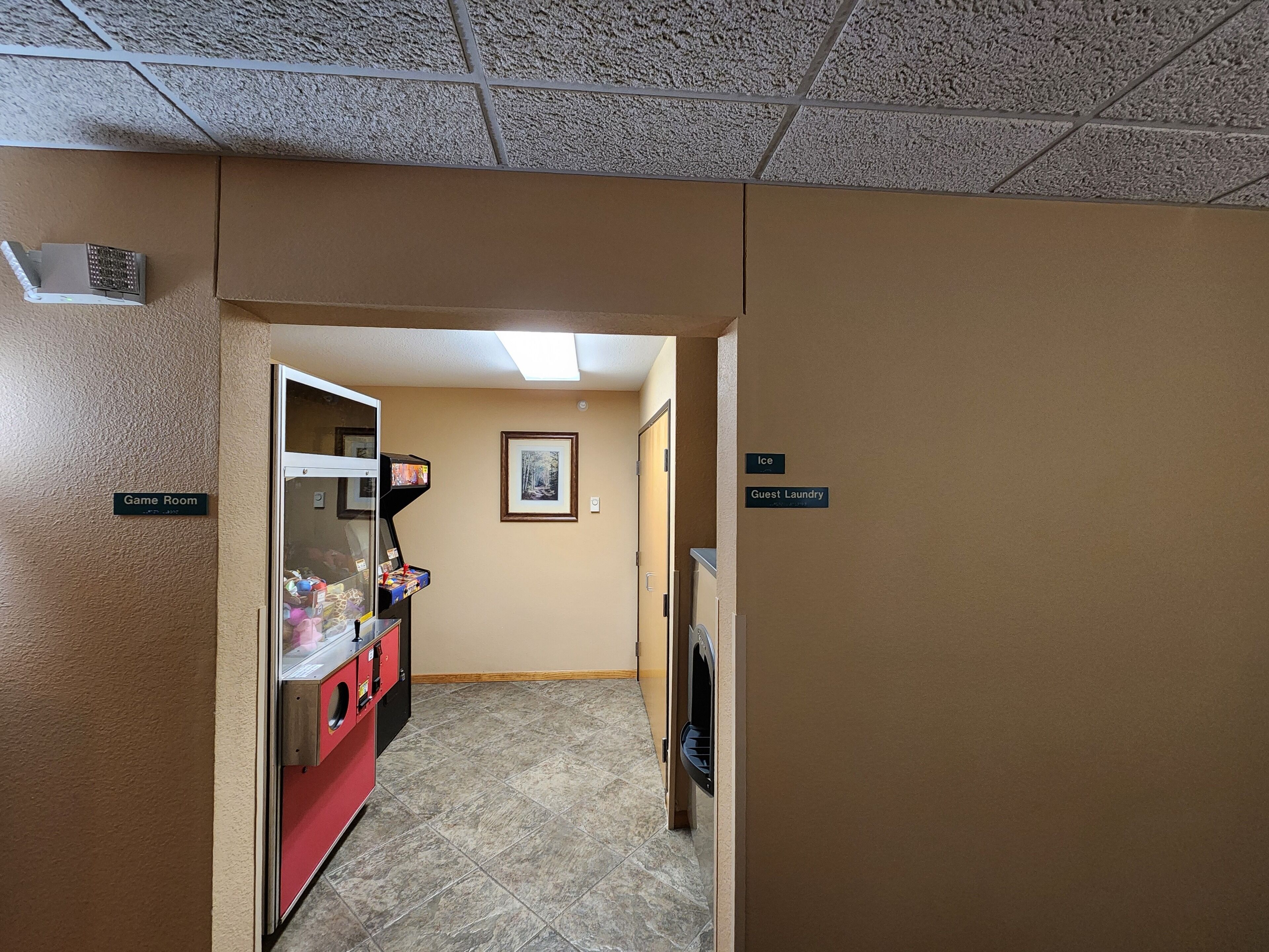 Een hotelgang met een speelkamer, een bord met ijs en gastenwasserij, en een lijst met een afbeelding aan de muur.