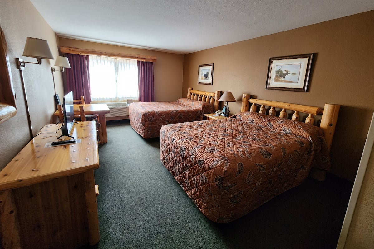 A hotel room with two beds, a desk with a computer, a chair, and a window with curtains.