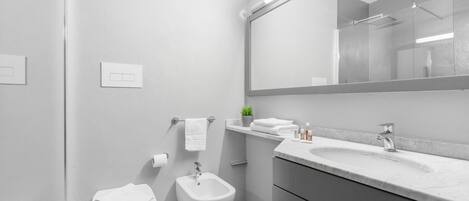 A modern bathroom with a toilet, bidet, vanity with a mirror, and a shower area.