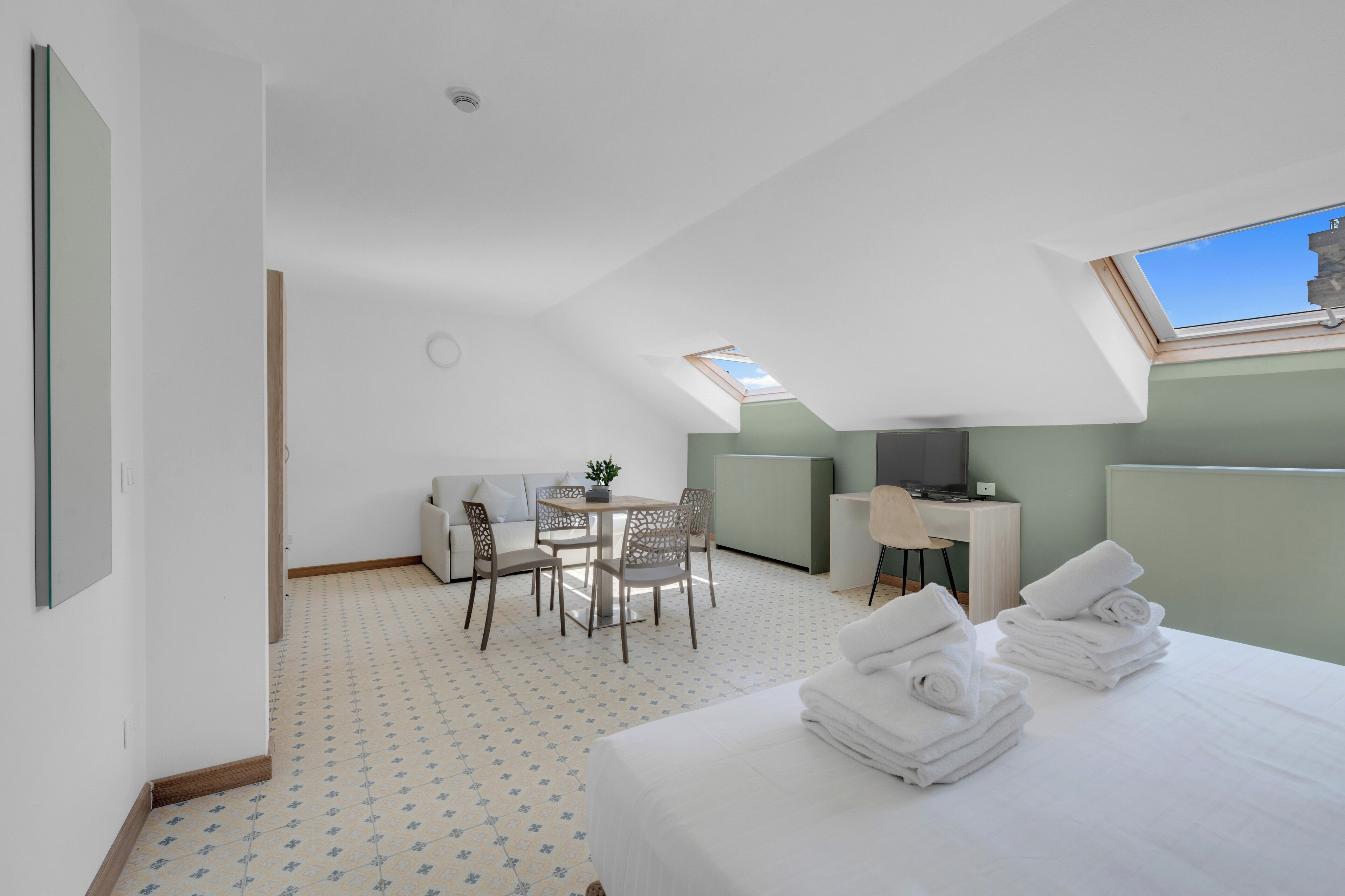 Una habitación de hotel con cama, escritorio, silla, mesita y sofá.