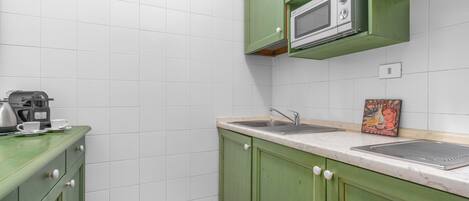 Una cocina con gabinetes verdes, azulejos blancos, un microondas y una cafetera.