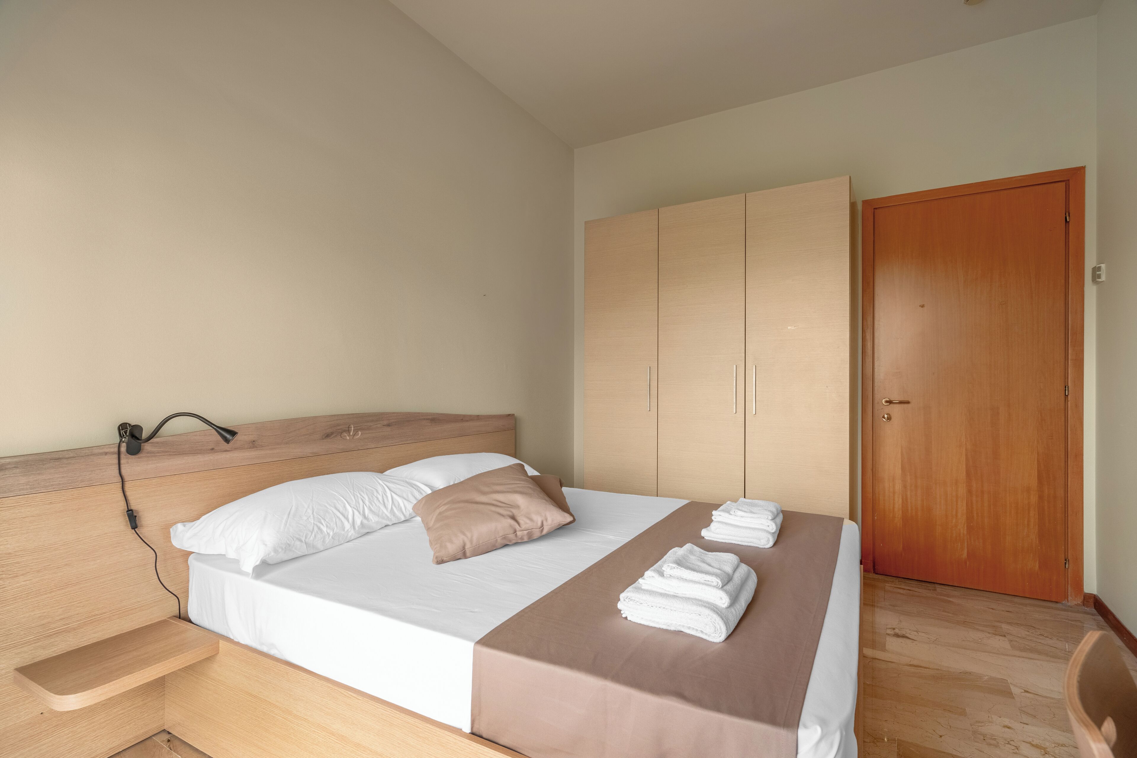 Una cama bien hecha con cabecera de madera, una mesita de noche y un armario con puertas correderas.