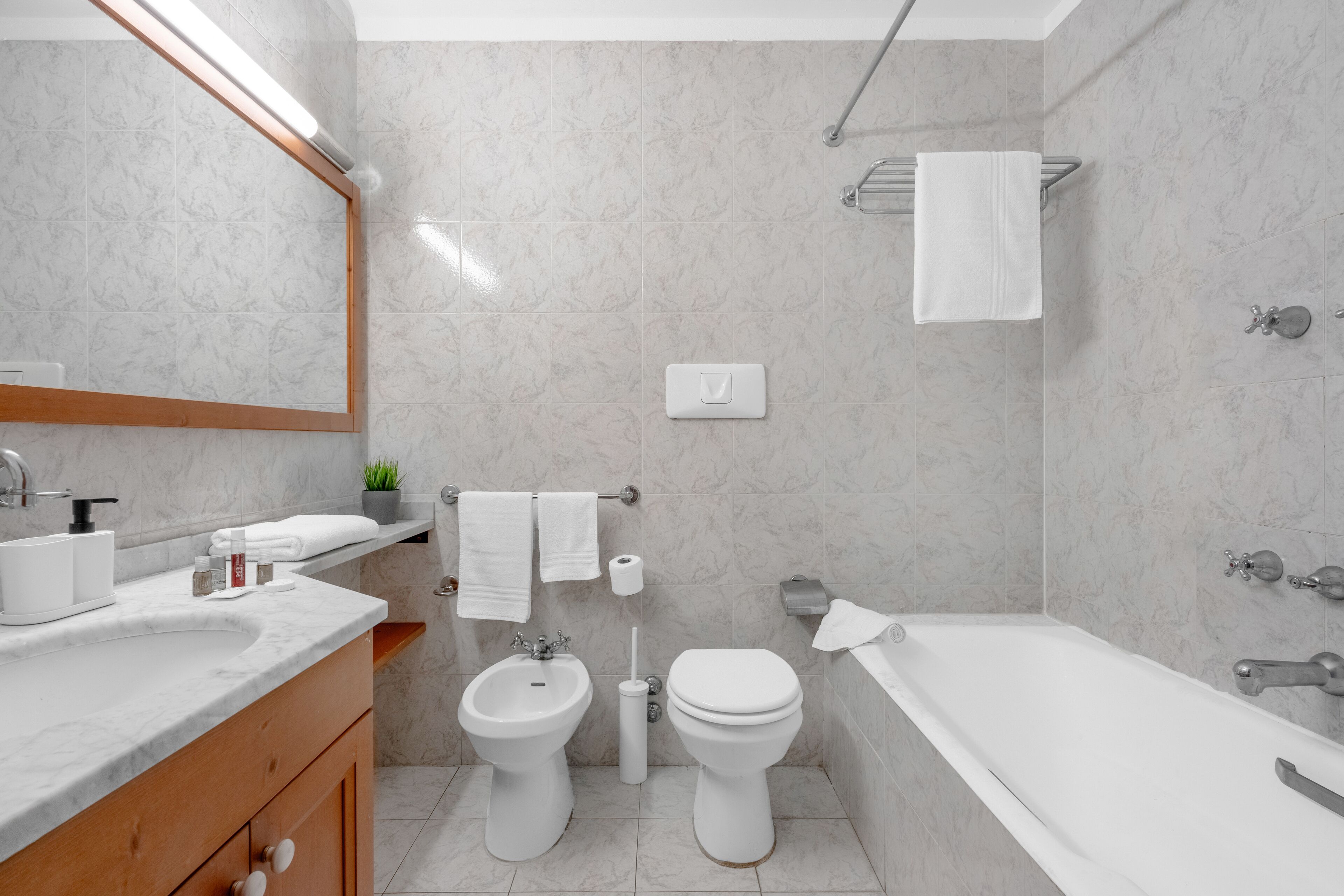 A modern bathroom with a marble sink, bidet, toilet, and bathtub.