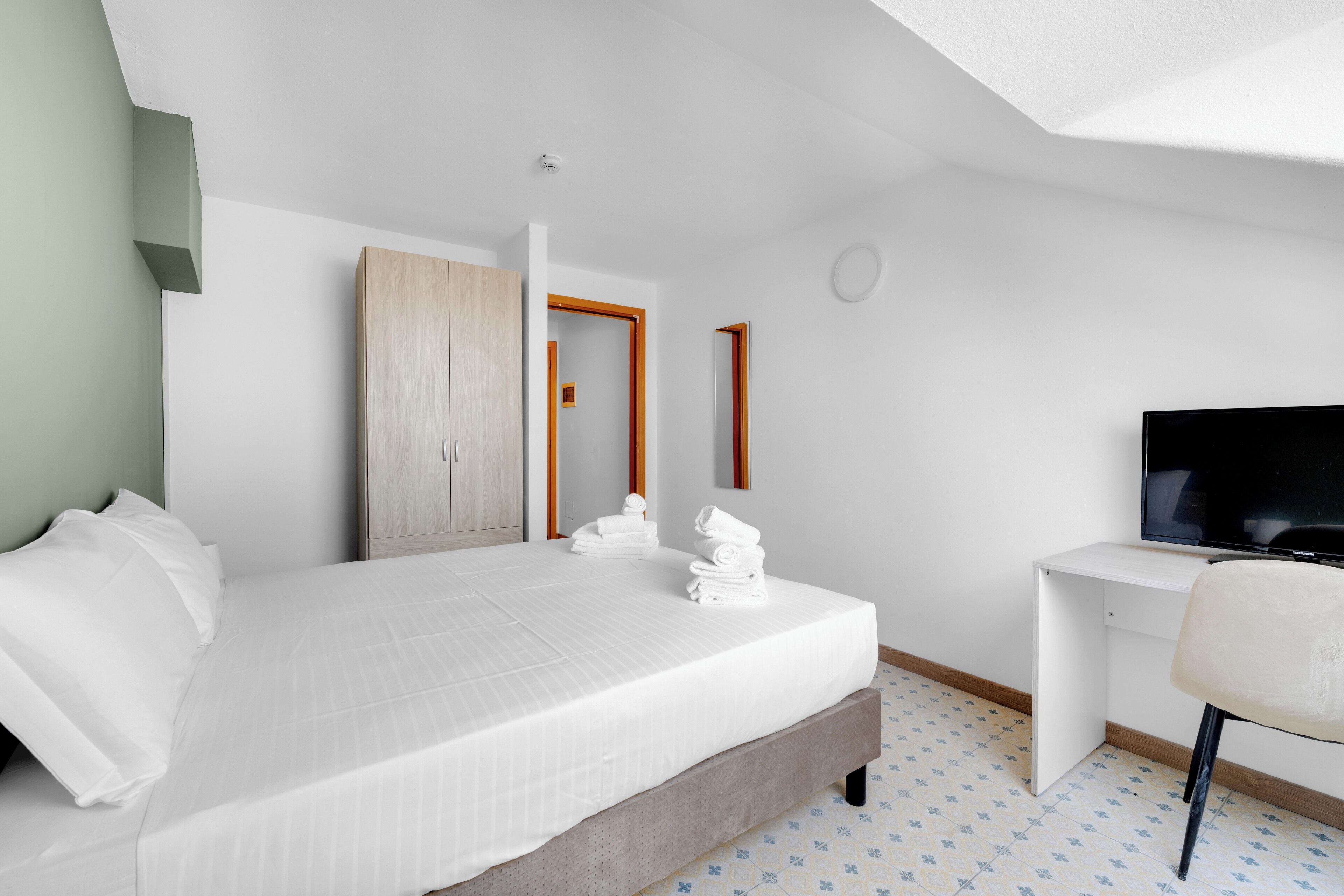 Habitació d'hotel amb llit, escriptori, televisió i armari.