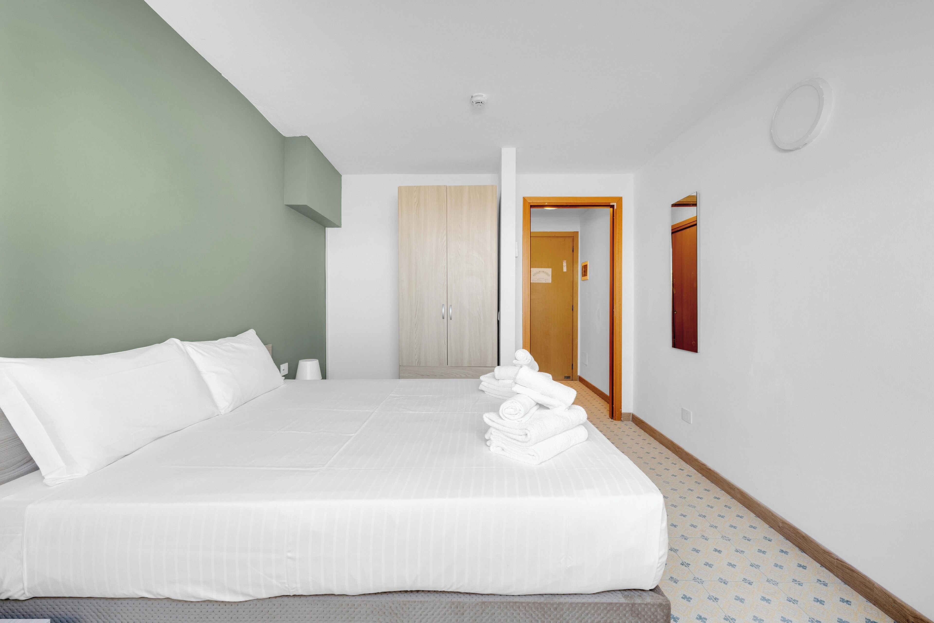 Habitación de hotel con una cama grande, un armario de madera, una puerta de baño y un espejo en la pared.
