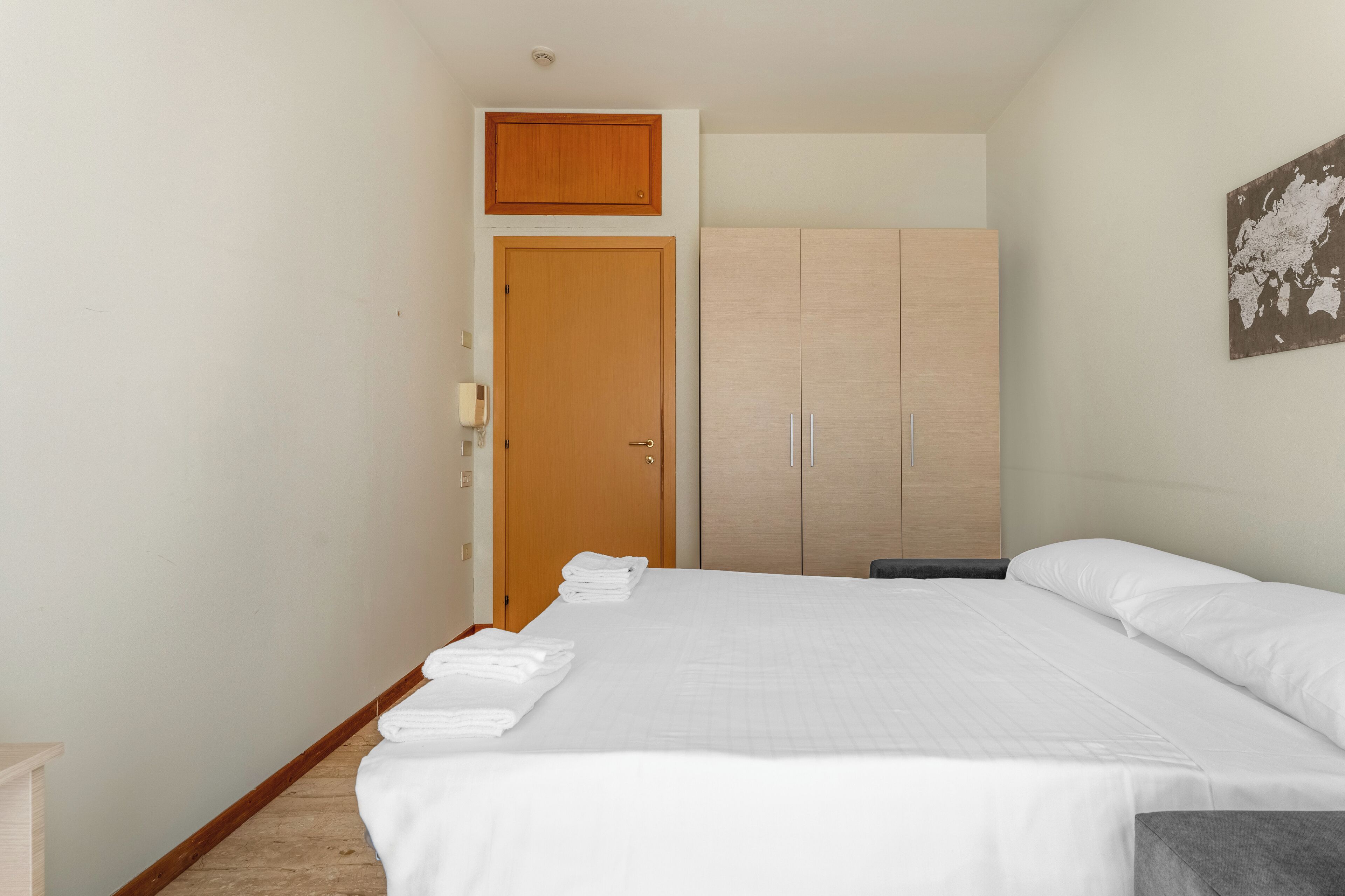Een hotelkamer met een groot bed, een houten garderobe en een kaart aan de muur.