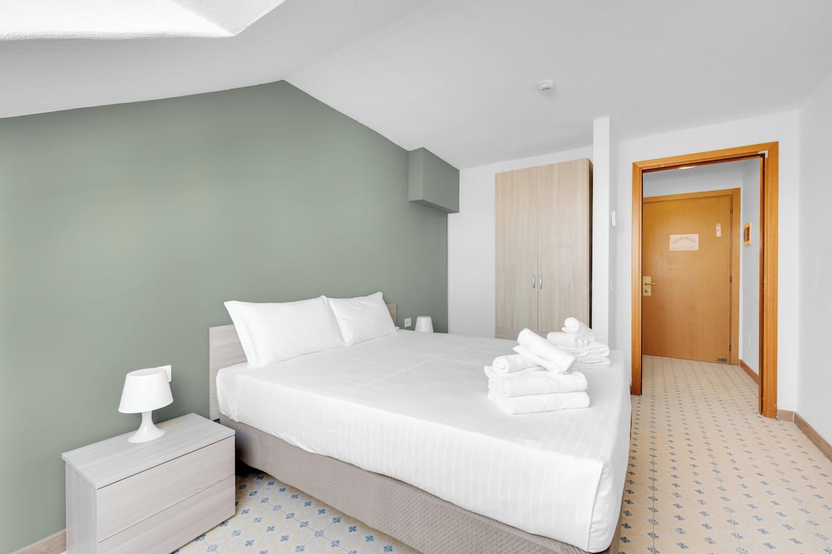 A neatly arranged hotel room with a bed, a nightstand, a wardrobe, and a door leading to another room.