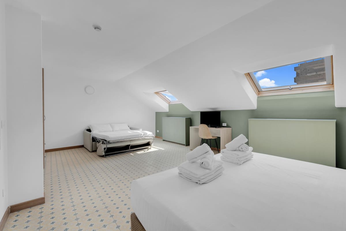 A modern hotel room with a bed, a desk, a chair, and a skylight.