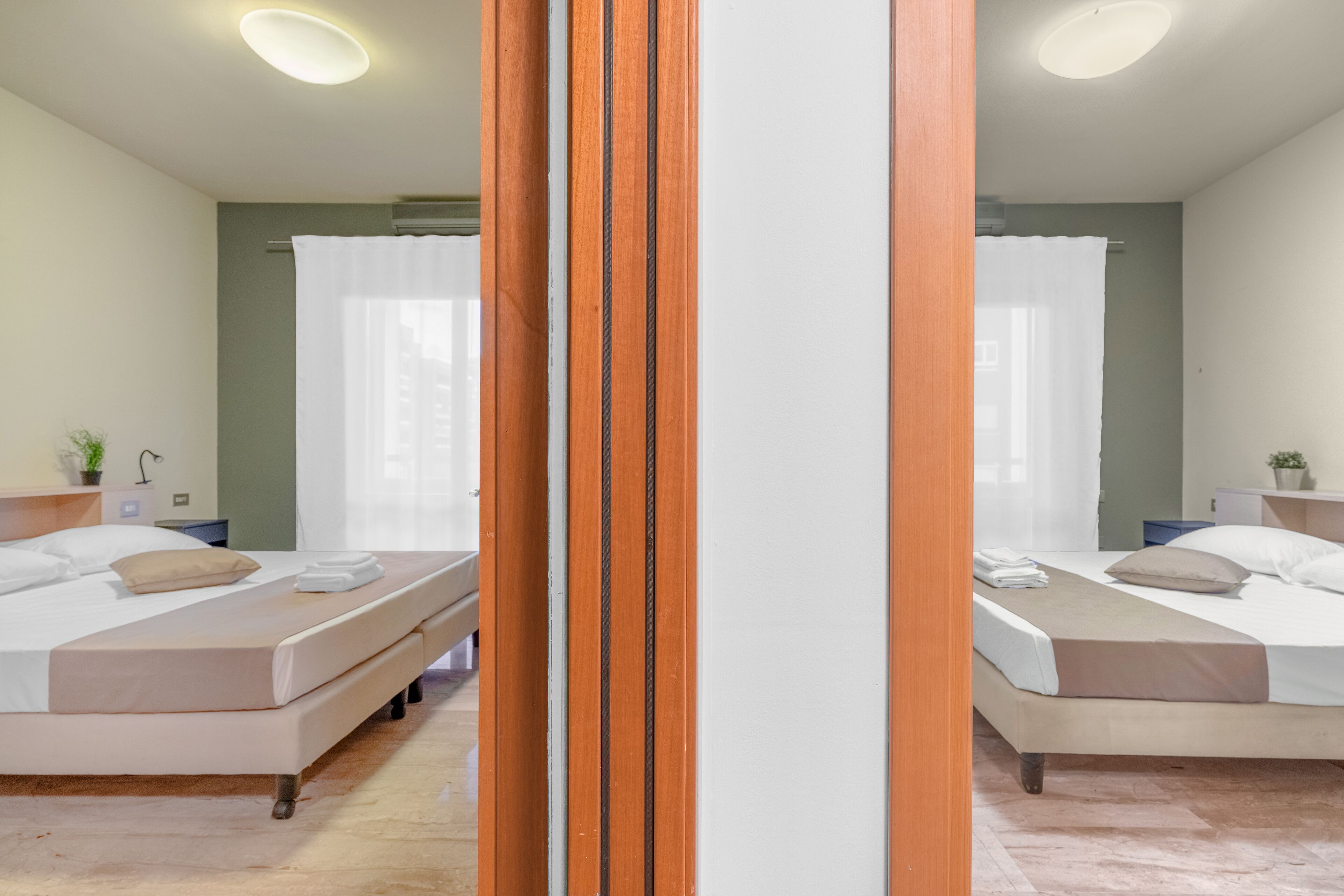 A hotel room with two beds, a wooden partition, and a view of the city.