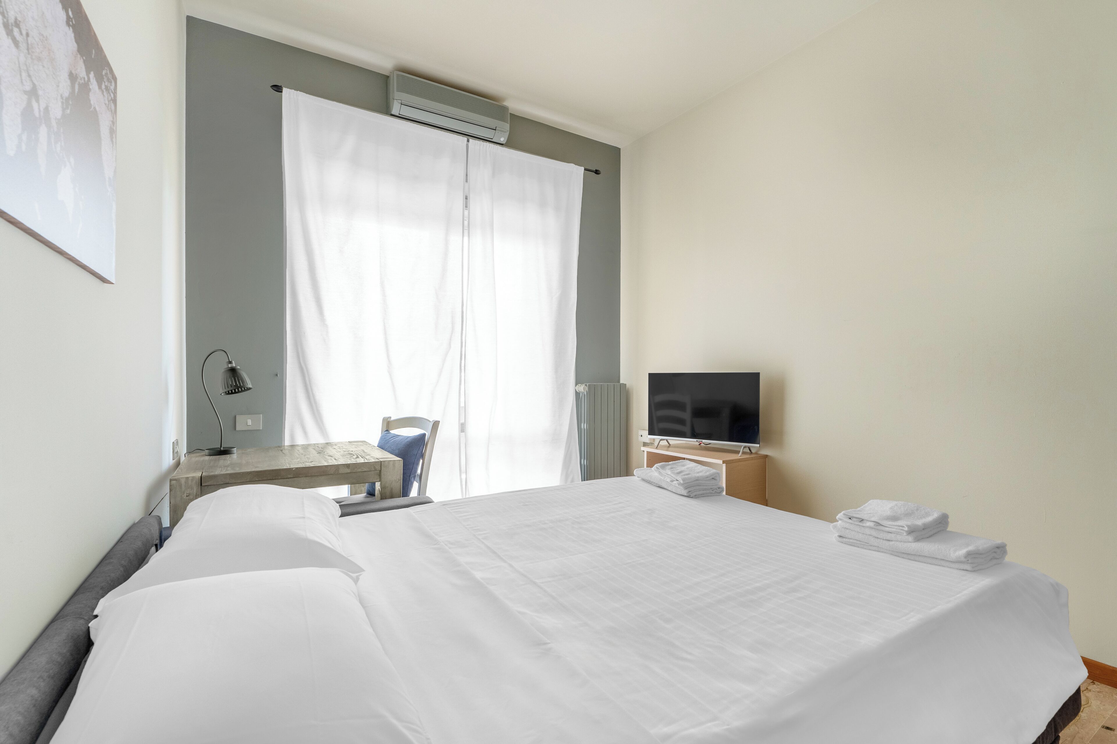 Habitación de hotel con una cama grande, un escritorio con lámpara, televisión y ventana con cortinas.