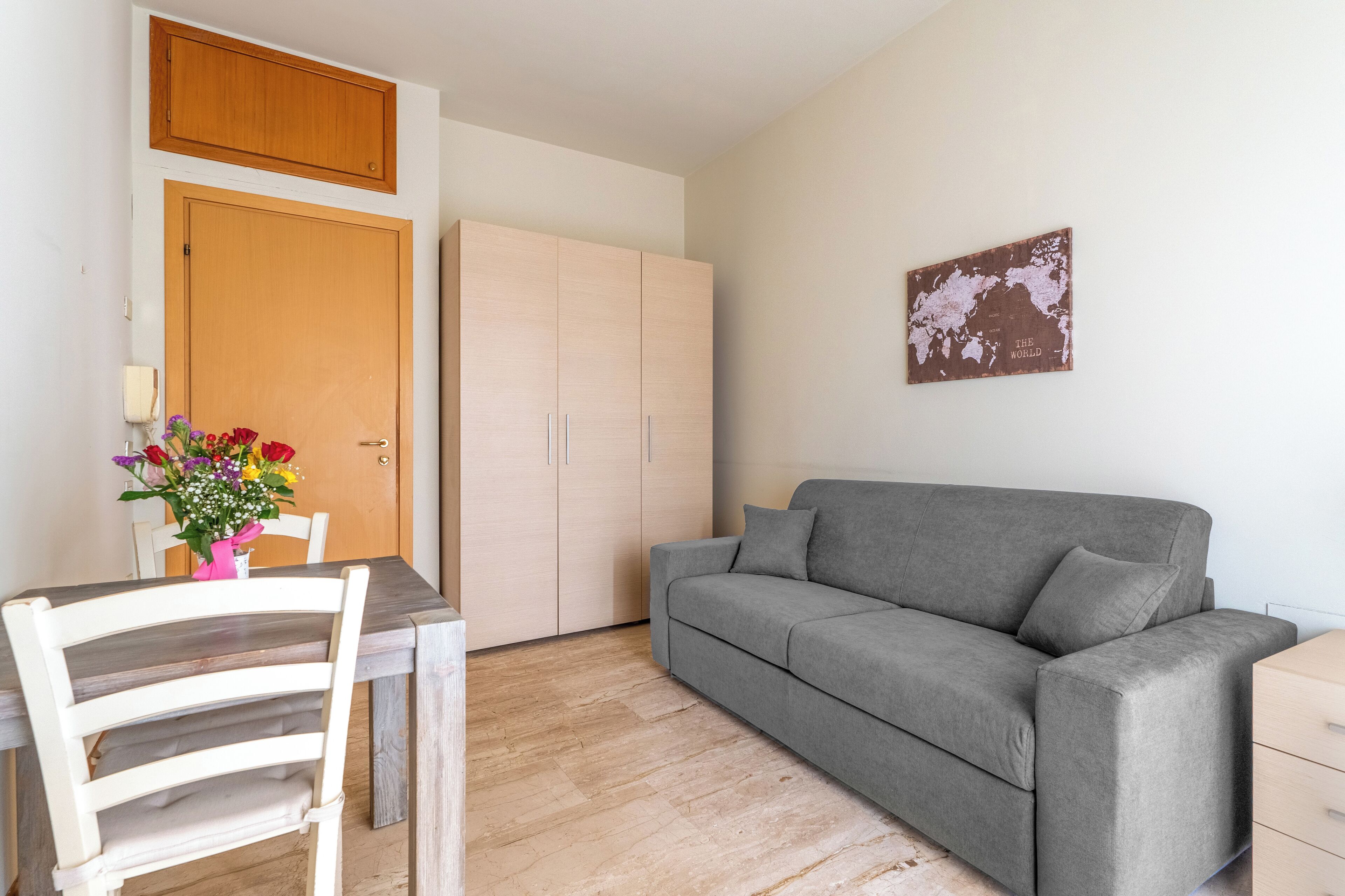 A room with a grey sofa, a wooden cabinet, a wooden door, and a wall-mounted map.