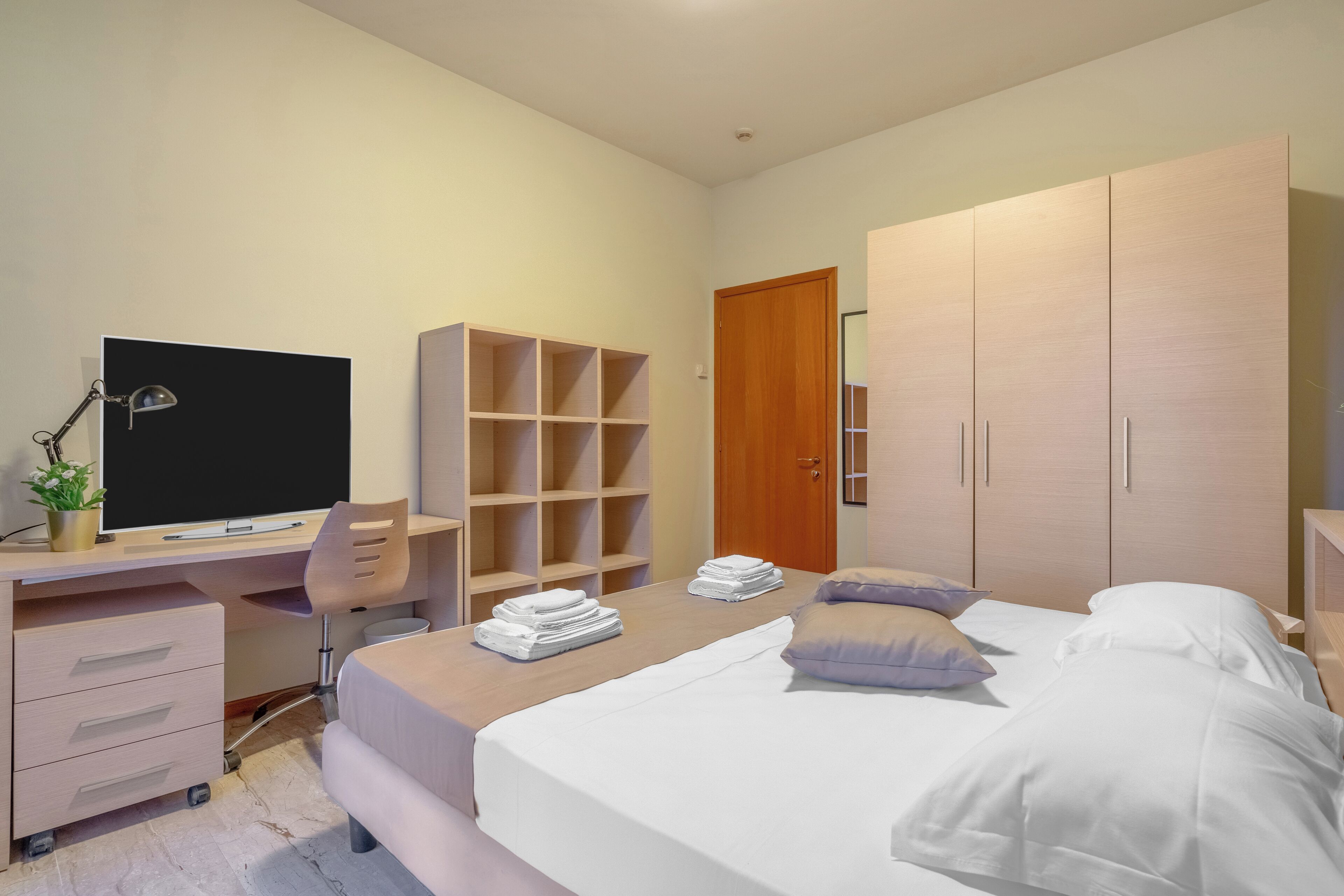A modern bedroom with a bed, a desk with a computer, a chair, and a wardrobe.