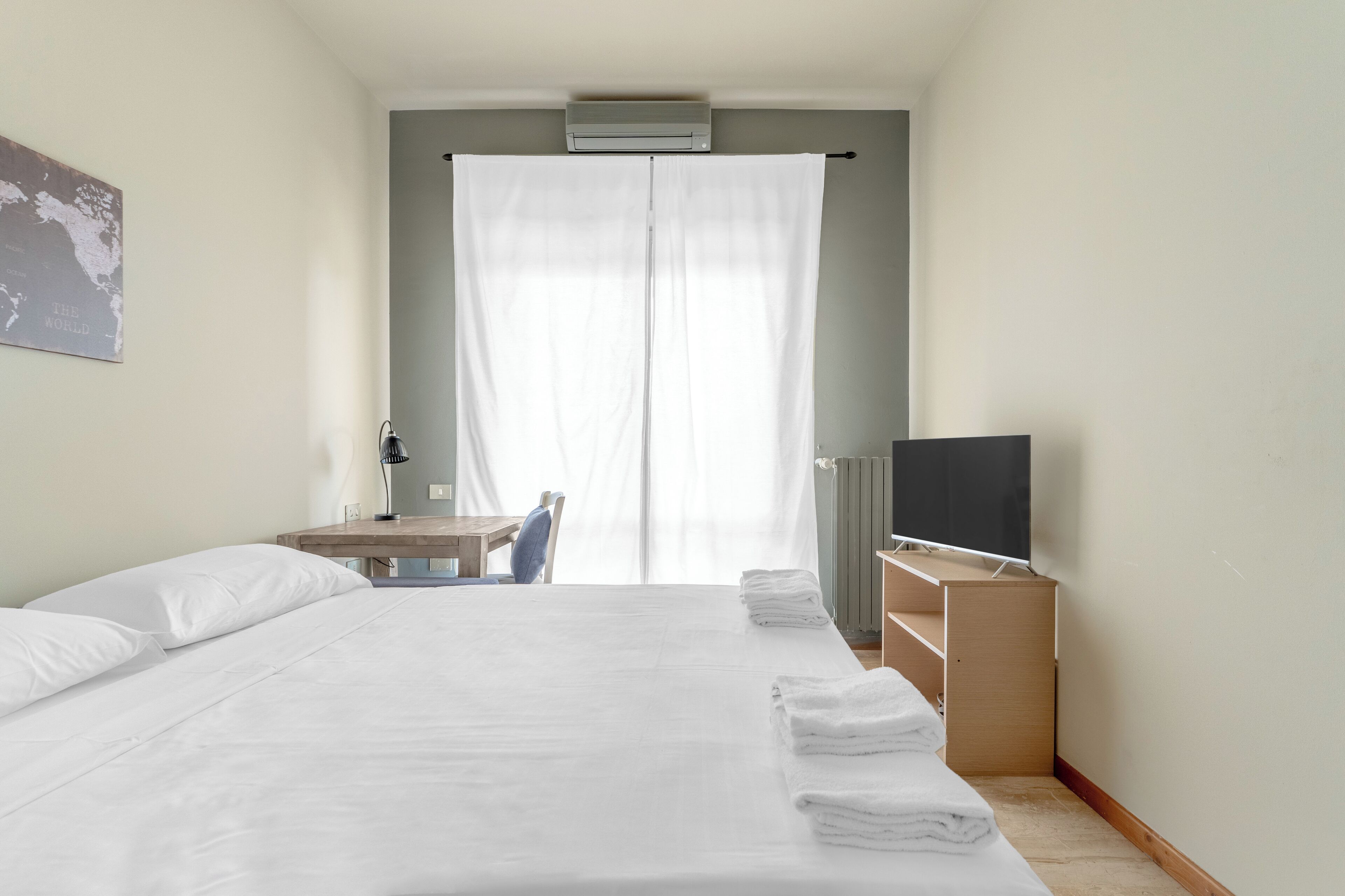 Quarto de hotel com cama, escrivaninha, cadeira, televisão e radiador.