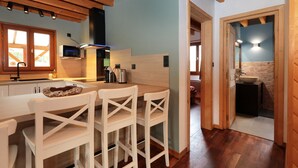A modern kitchen with wooden beams, a microwave, and a sink. There are white chairs and a wooden table.