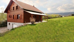 A wooden house with a sloped roof, a porch, and a grassy yard.