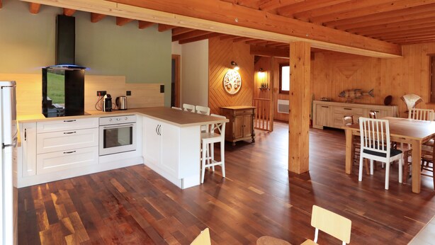 A spacious kitchen with wooden beams, a central island, and a dining area with chairs and a table.