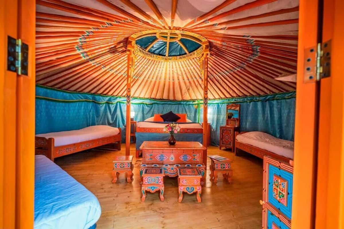 Een traditioneel yurt-interieur met een centraal bed, twee kleinere bedden en een houten tafel met banken.