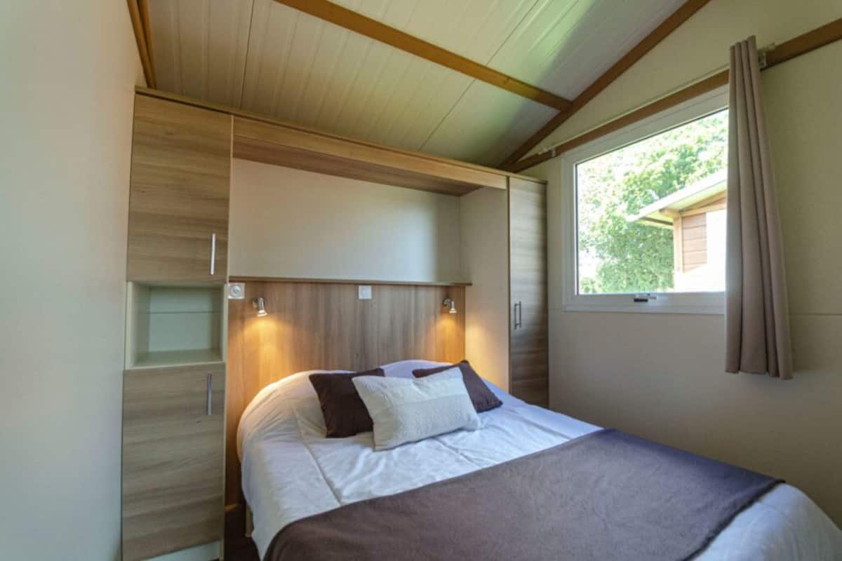 Een kleine slaapkamer met een bed, een inbouwkast en een raam met gordijnen.