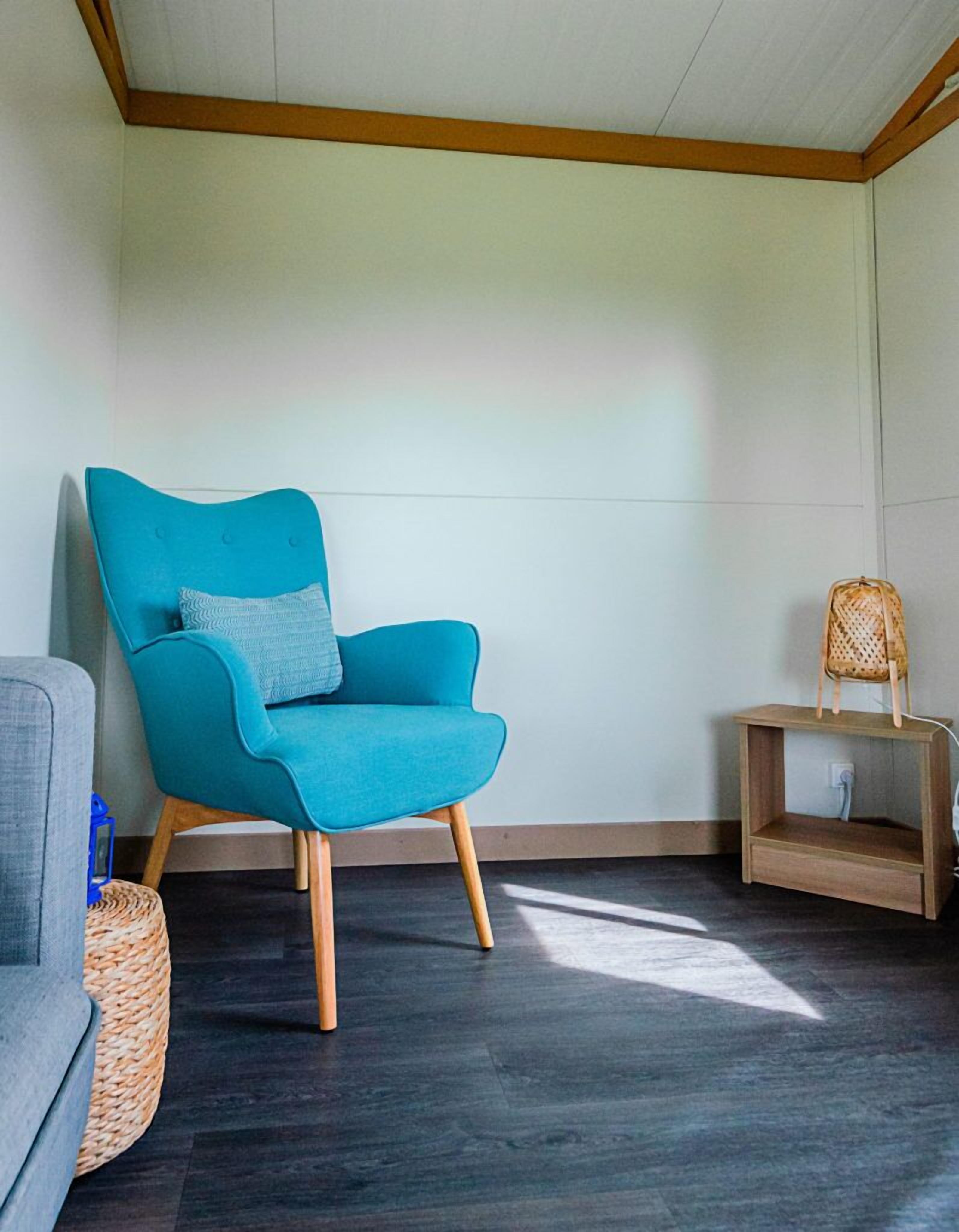 Una habitación con un sillón azul verdoso, una pequeña mesita de madera y un sofá gris.