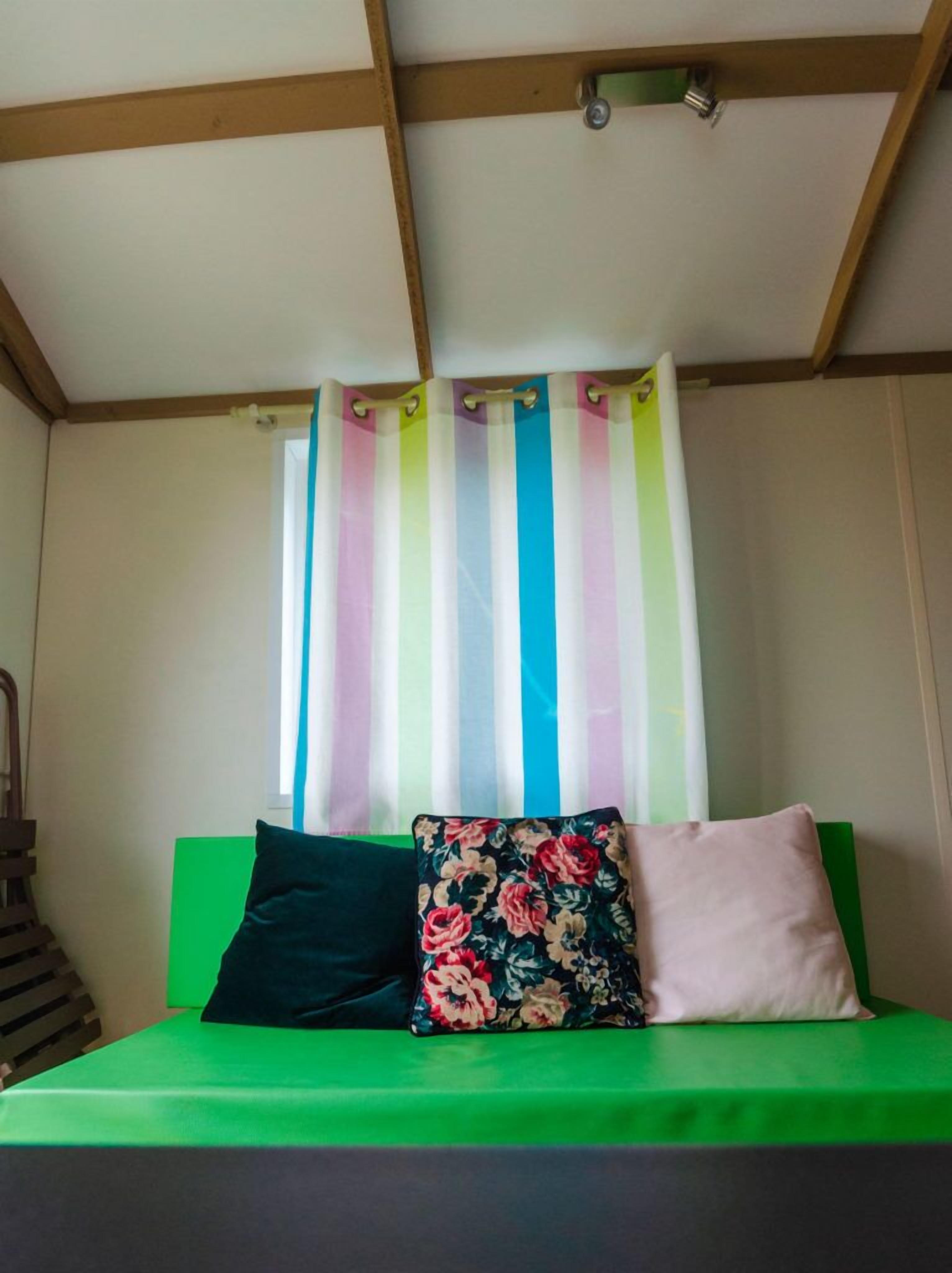 A room with a green sofa, two pillows, a striped curtain, and a wooden ceiling.