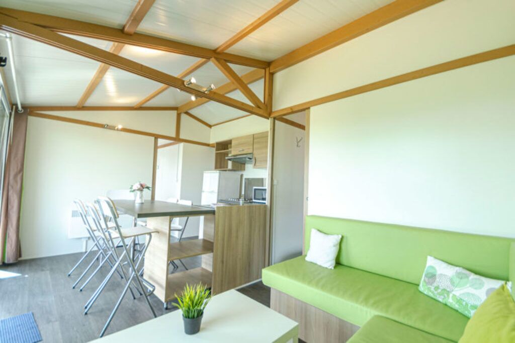 A modern interior with a dining area, a green sofa, and a kitchen in the background.