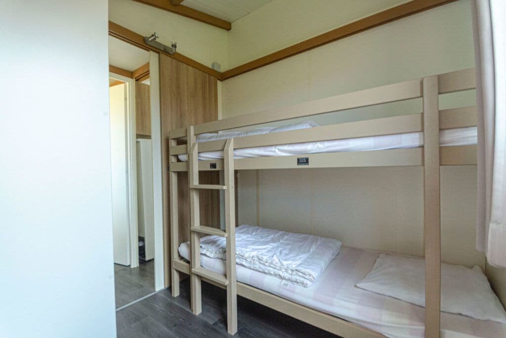 Une chambre avec un lit superposé, une échelle en bois, une porte et un sol carrelé.