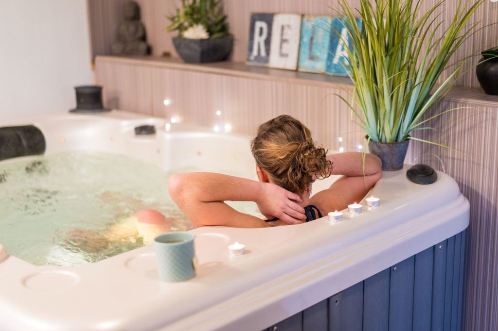 A person relaxing in a hot tub with a plant and decorative items in the background.