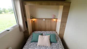 A small bedroom with a bed, two pillows, a window, and a wooden headboard.