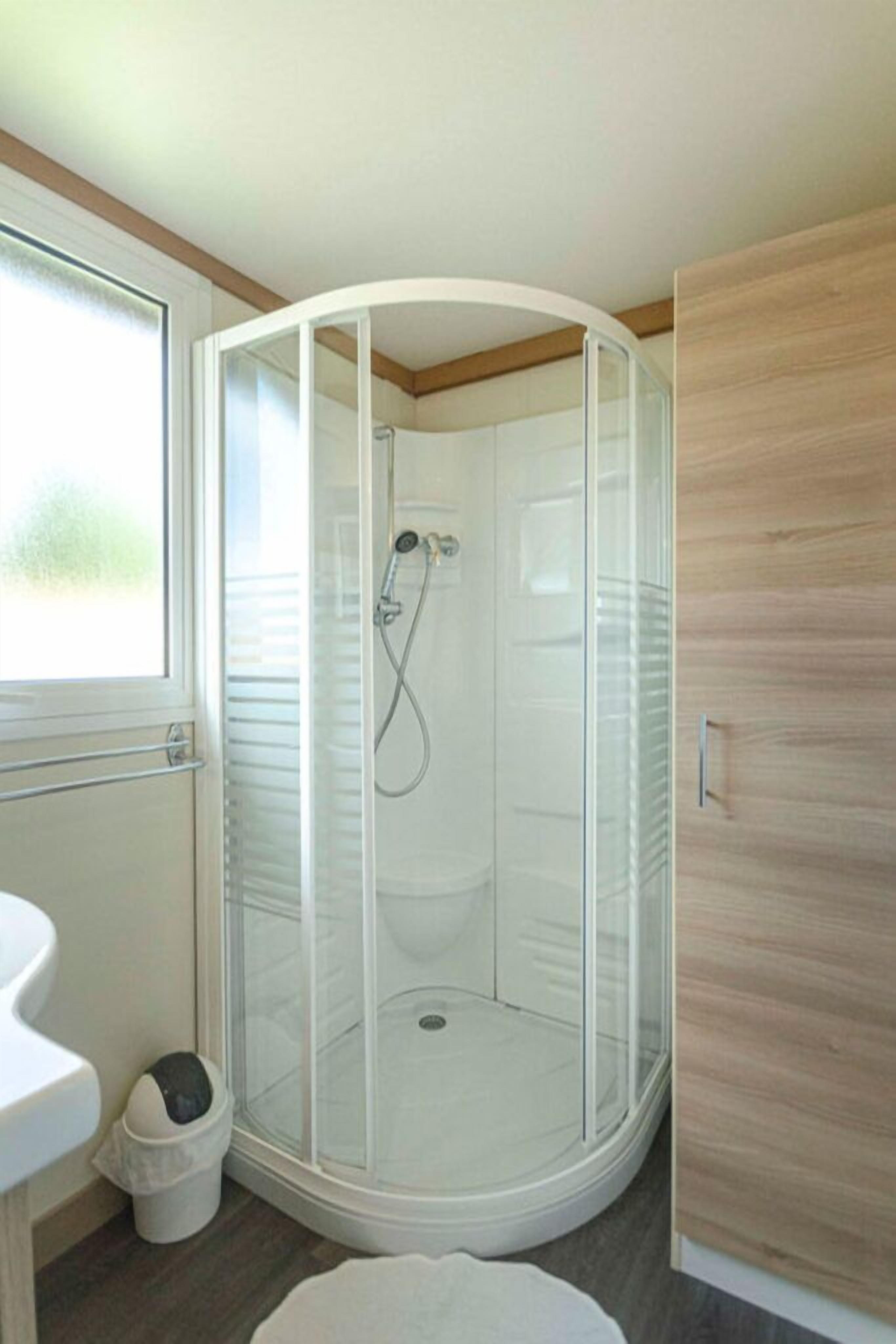 Ein modernes Badezimmer mit einer einteiligen Duschkabine, einem weißen Waschbecken und einem Holzschrank.